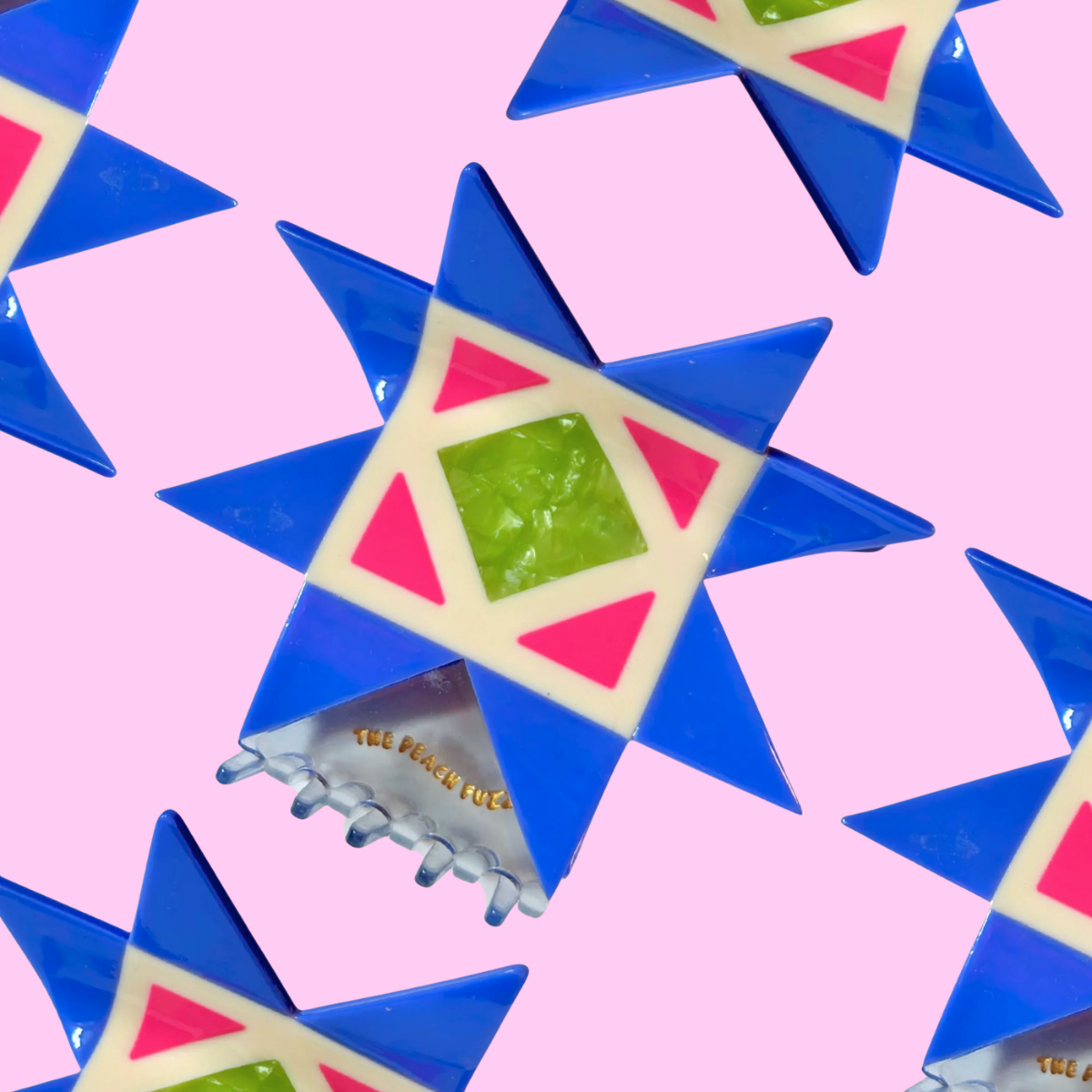 A close-up of a colorful geometric star-shapedclaw clip with blue, pink, green, and cream sections, arranged in a repeating pattern on a light pink background.