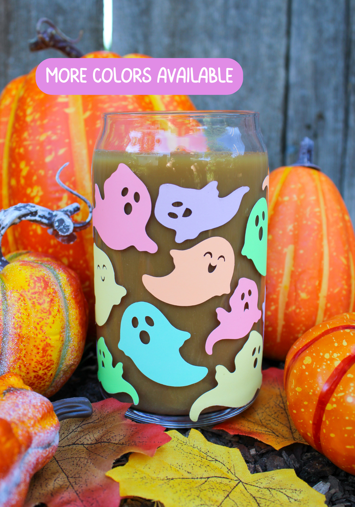 A glass tumbler with a colorful ghost pattern on a background of autumn leaves and pumpkins, indicating the product may glow in the dark.