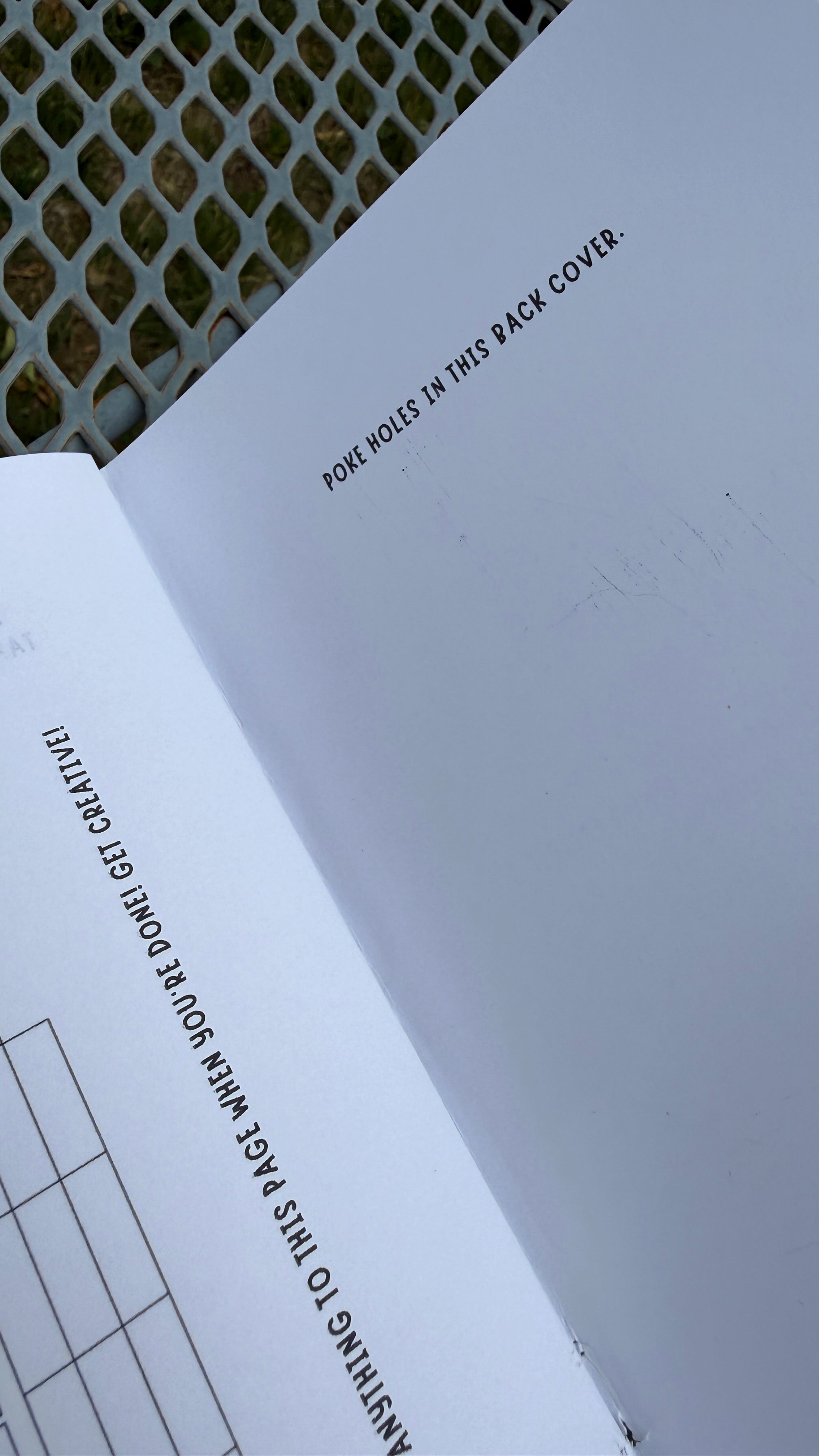 A close-up of an open white booklet or instruction sheet laid on a metal mesh surface, with printed text including 'POKE HOLES IN THIS BACK COVER.' and a small grid diagram.