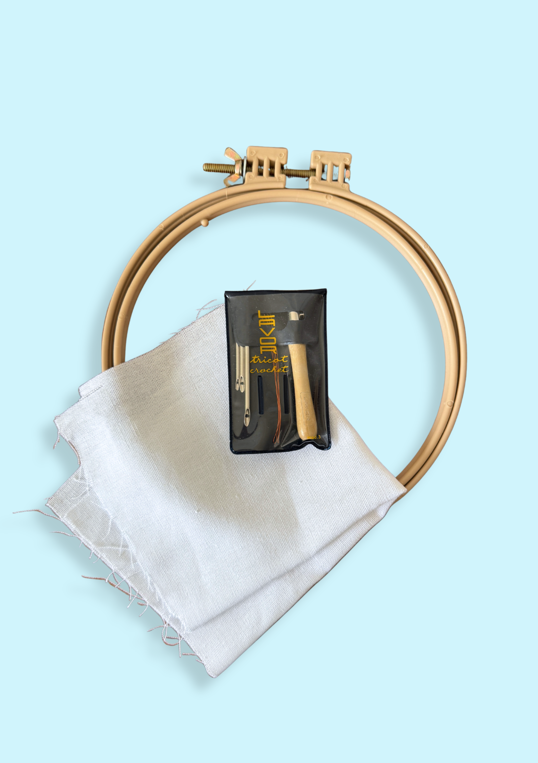 An embroidery hoop, punch needle, and fabric on a light blue background