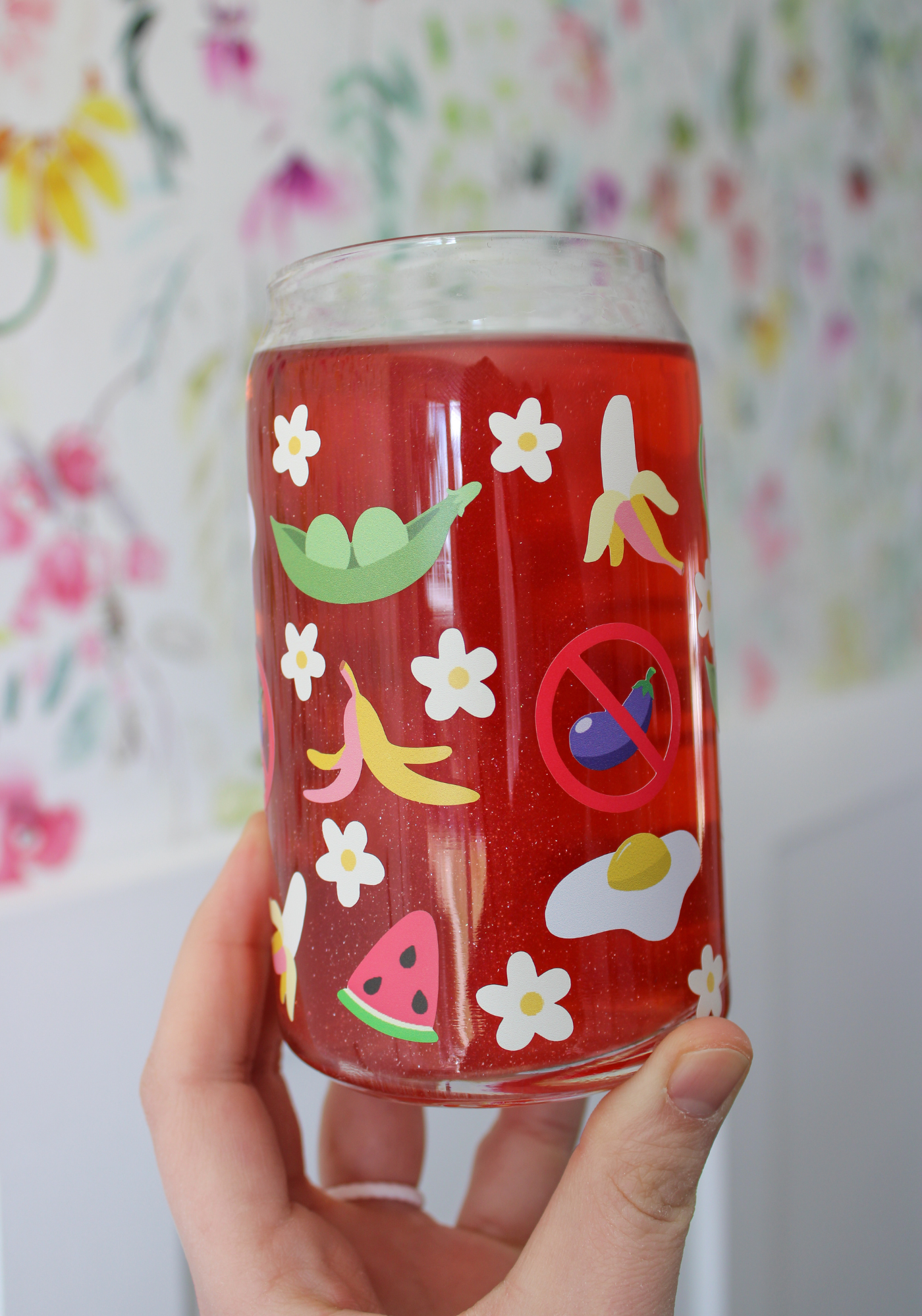 Glass with food stickers held by a hand against a floral background