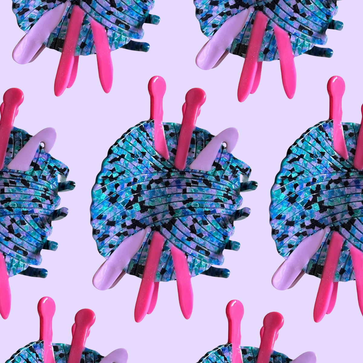 A repeating pattern of decorative hair claw clips on a light lavender background. Each clip features a textured, mosaic-like blue and black ball of yarn with bright pink and pale lavender knitting needles and crochet hook elements.