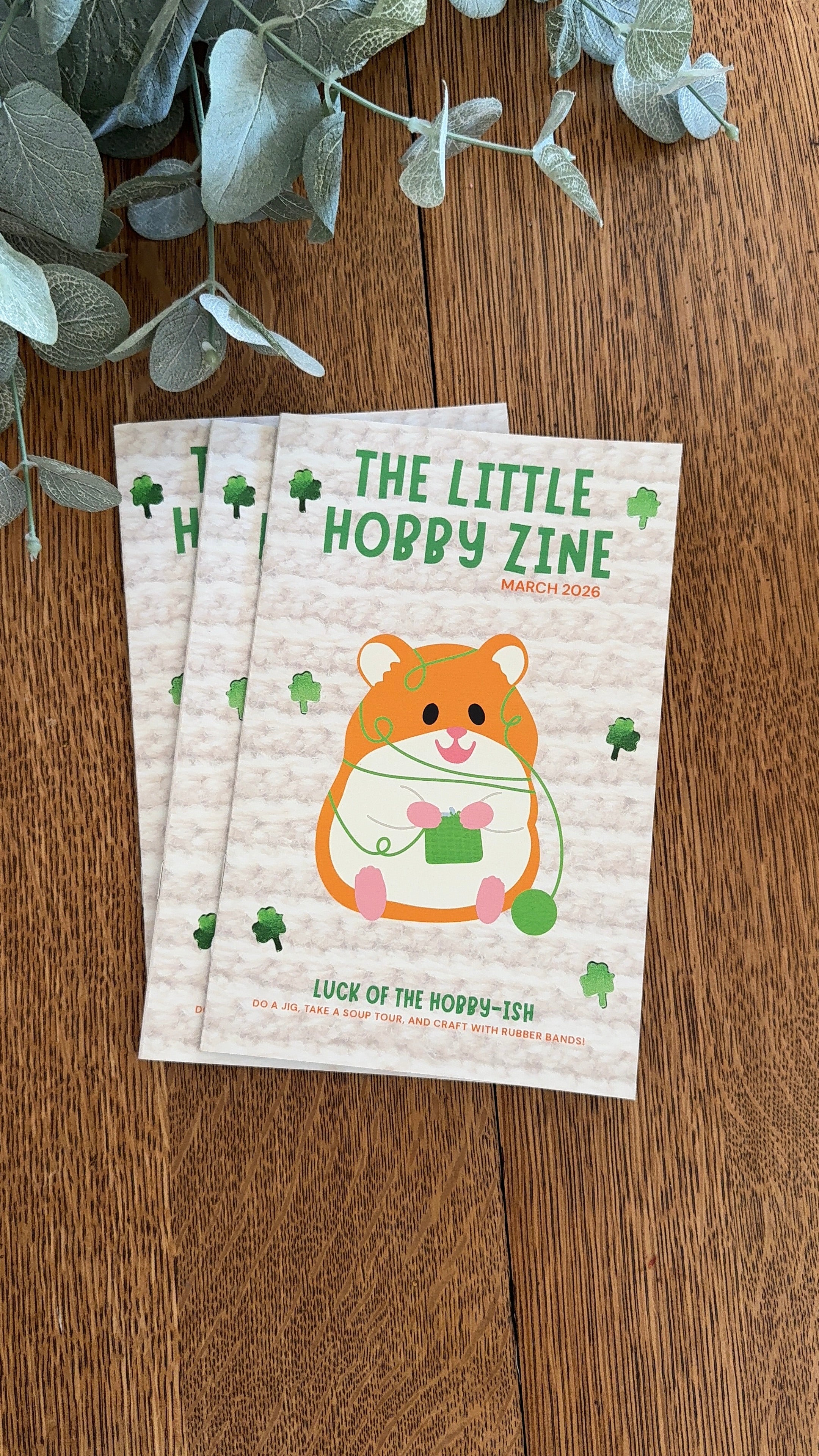 Two copies of 'The Little Hobby Zine' on a wooden surface with greenery.