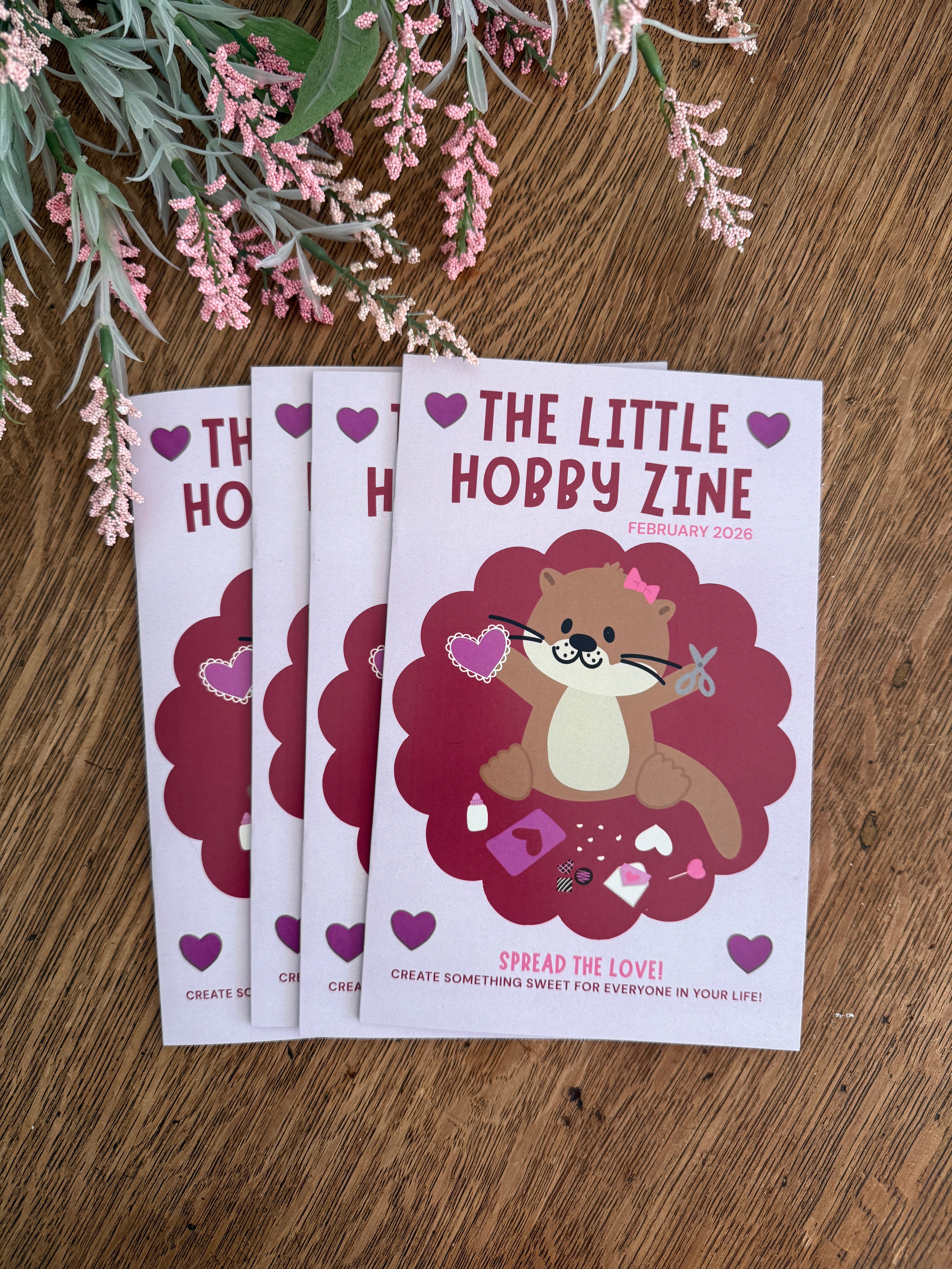 Three zines titled 'The Little Hobby Zine' on a wooden surface with flowers.