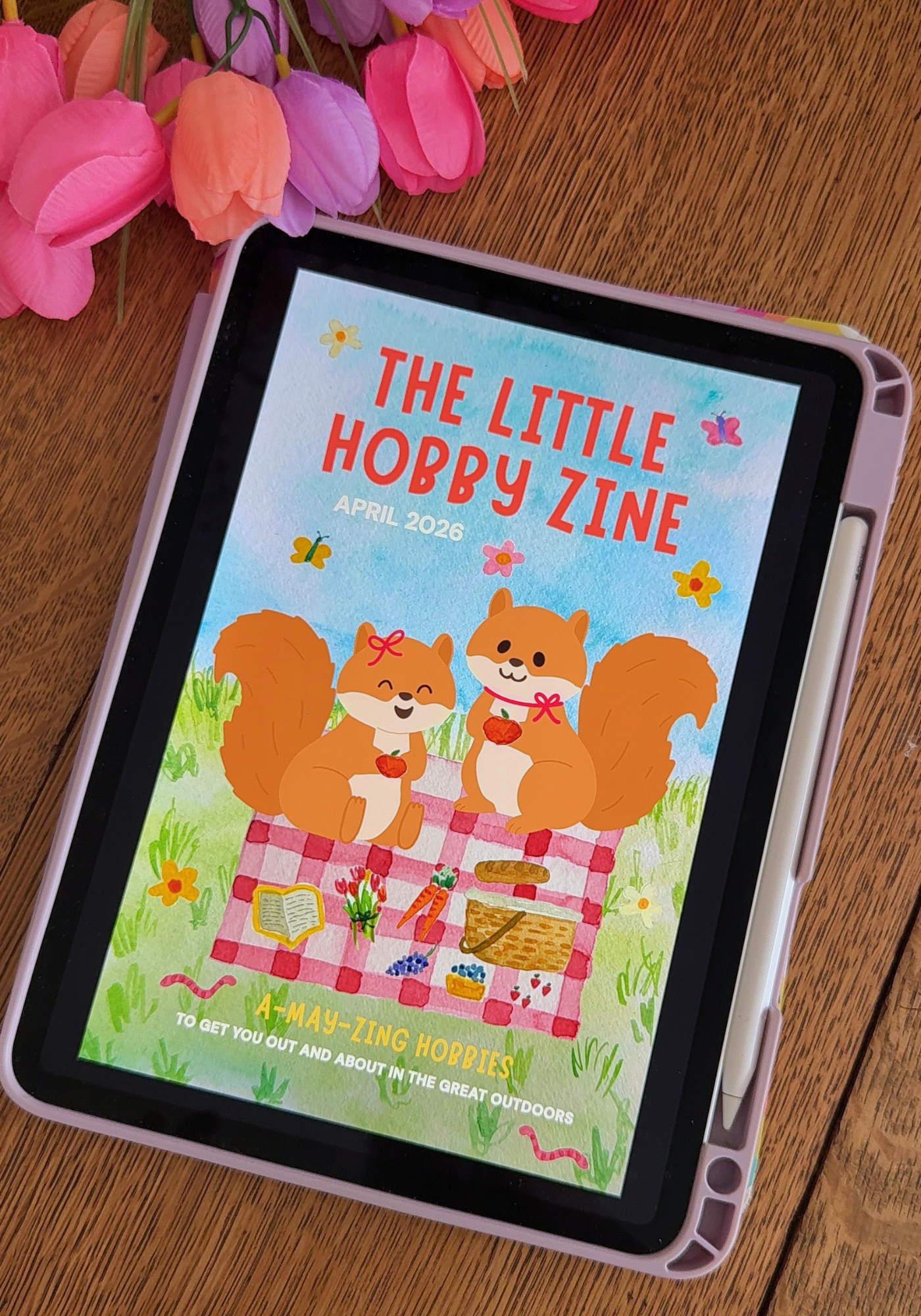 E-reader displaying 'The Little Hobby Zine' on a wooden surface with flowers.