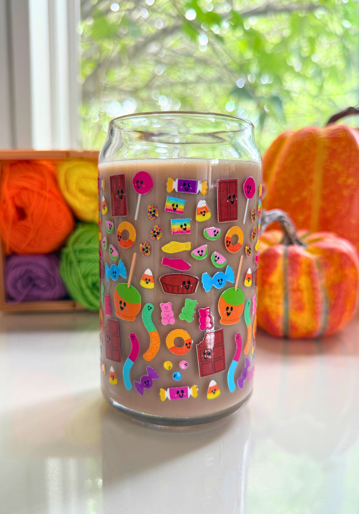 Glass can with colorful pieces of candy design on a white surface with pumpkins and yarn in the background