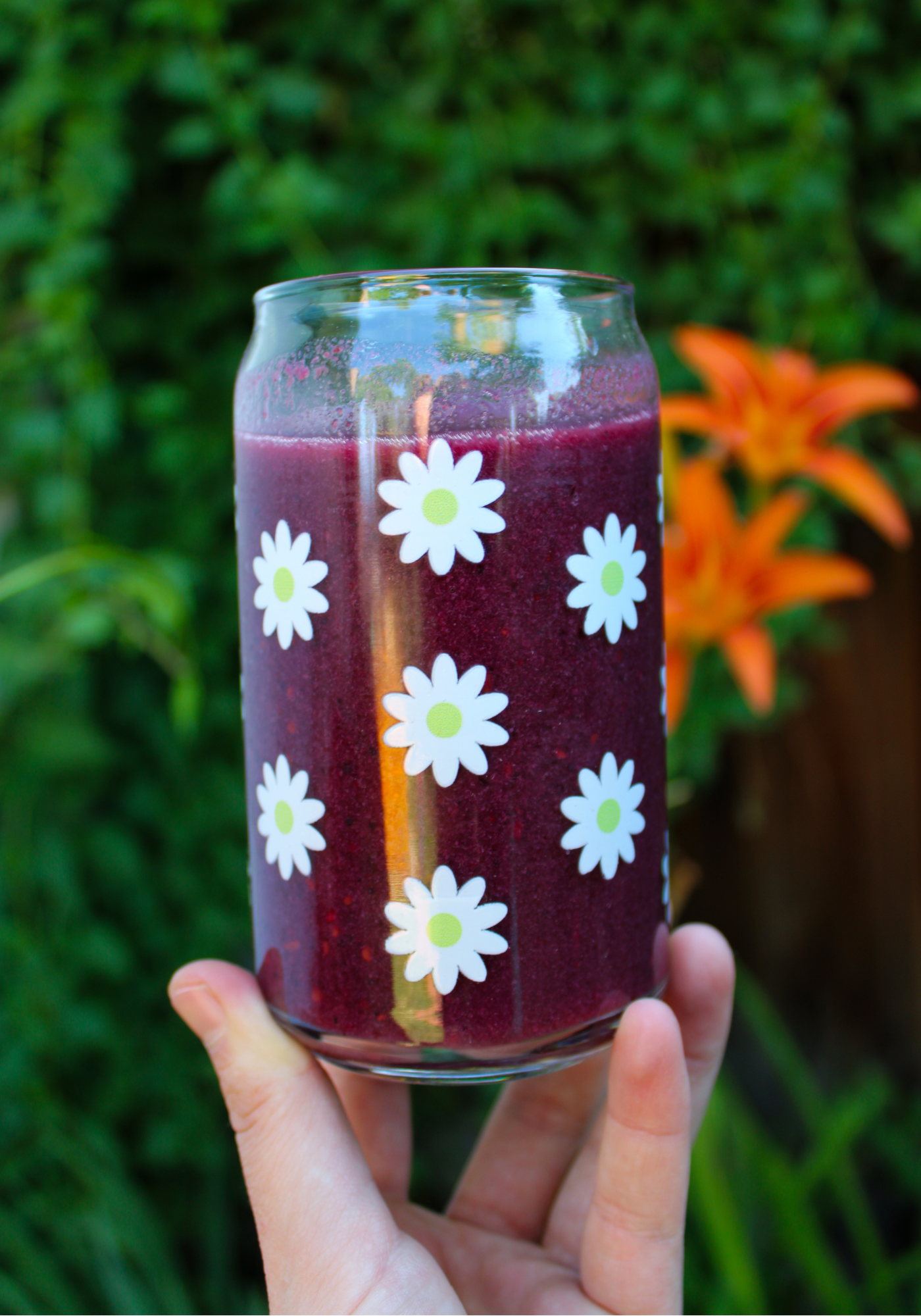 Hand holding glass can with scattered white daisies in front of a blurry plant background